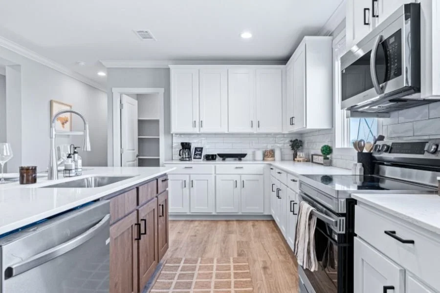 Modern kitchen with white cabinets, stainless steel appliances, wood flooring, and a white countertop island.
