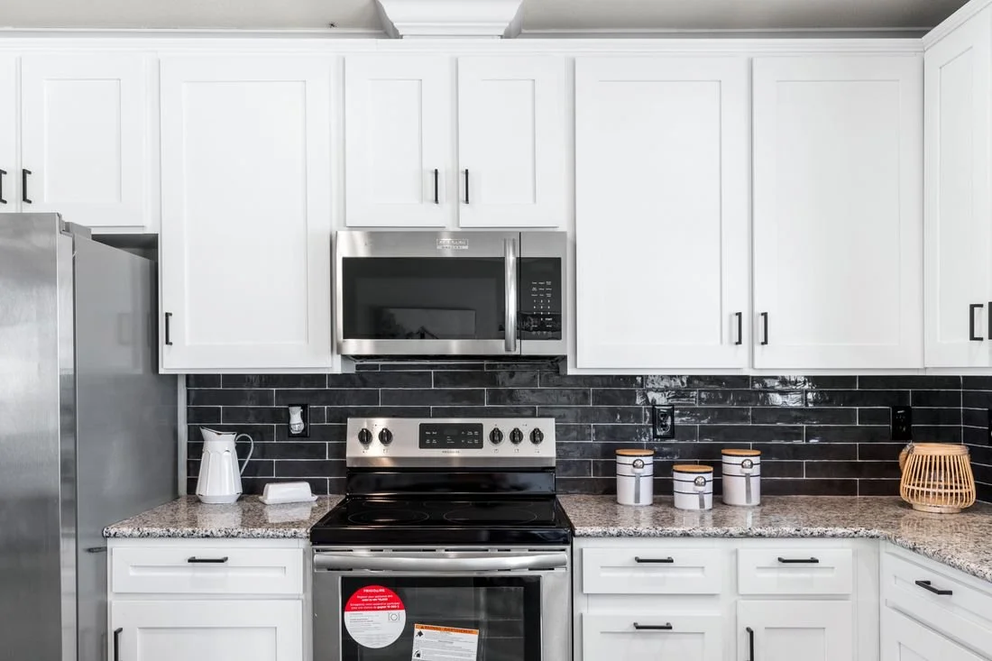 Modern kitchen with white cabinets, black backsplash, stainless steel microwave, electric stove, and granite countertops.
