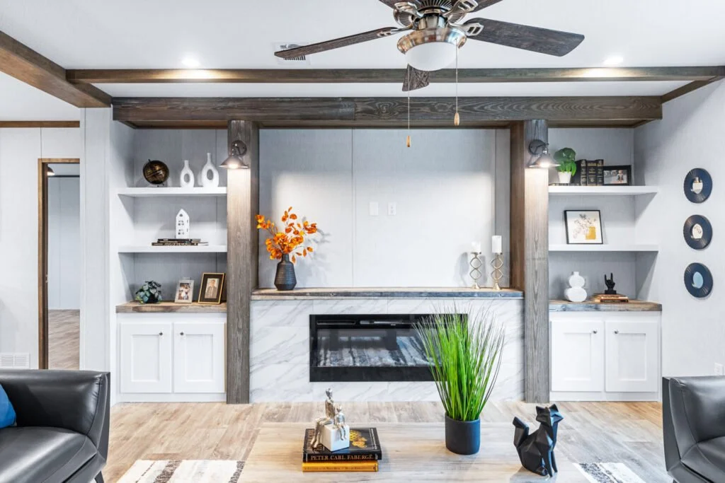 Living room with a modern fireplace, wooden and white shelves with decorative items, a green plant, and a ceiling fan.
