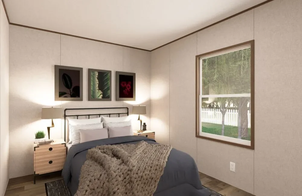 A cozy bedroom with a bed, two nightstands with lamps, and three framed botanical pictures above the headboard. There is a large window showing a view of a yard with trees and a white fence.
