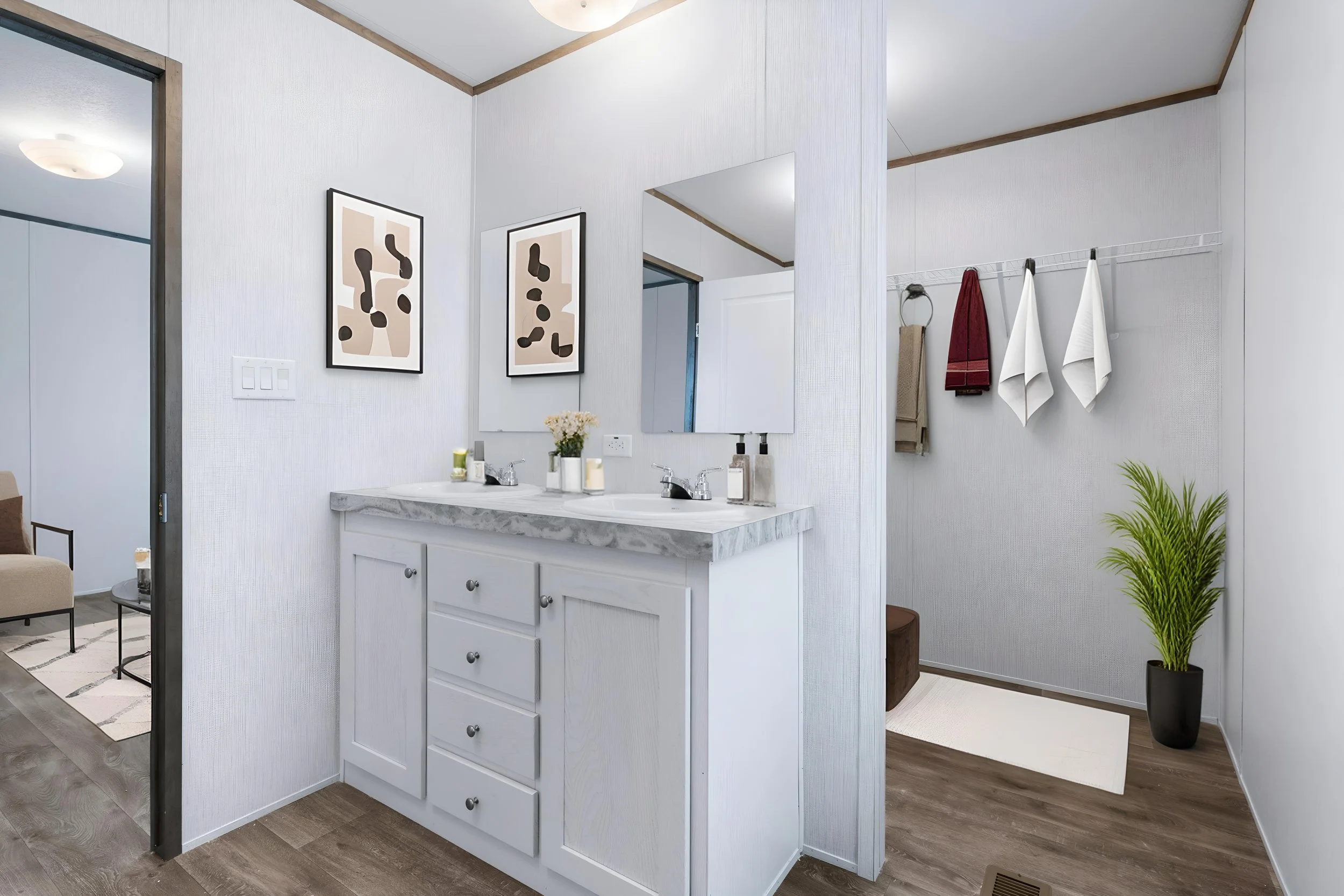 A bathroom with a white cabinet sink, a mirror, framed abstract art, hanging towels, and a potted plant in a black pot.