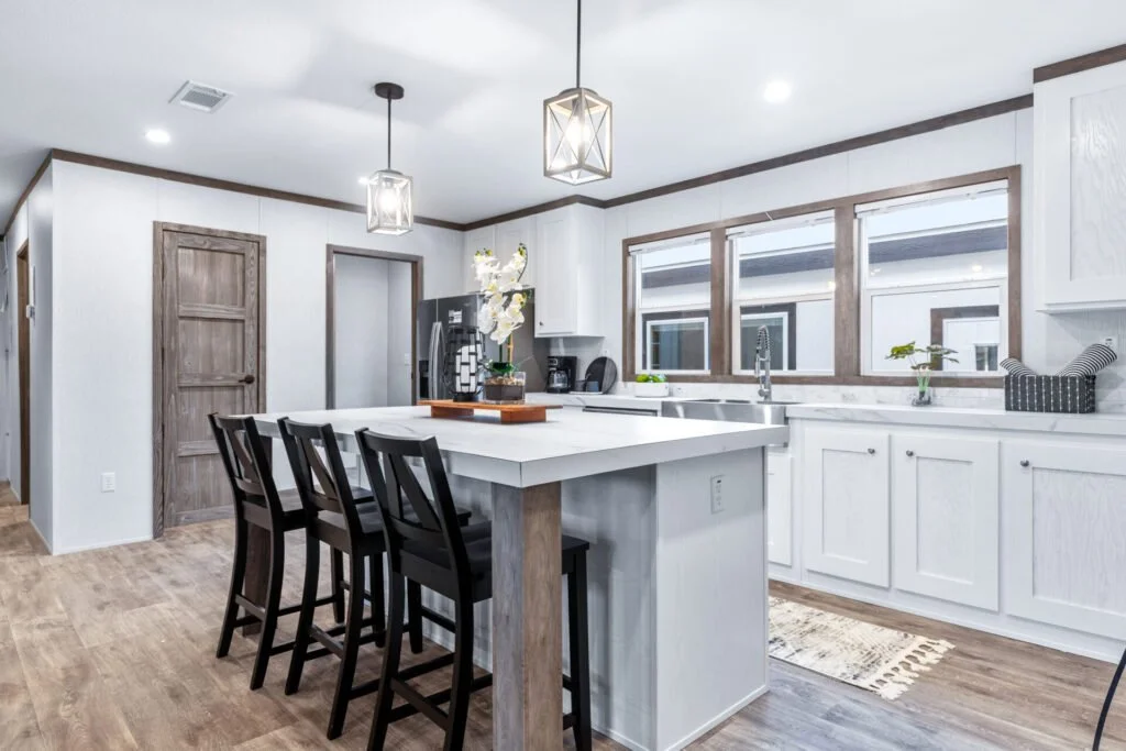 Modern kitchen with white cabinets, wooden accents, a kitchen island with bar seating, pendant lighting, and large windows.