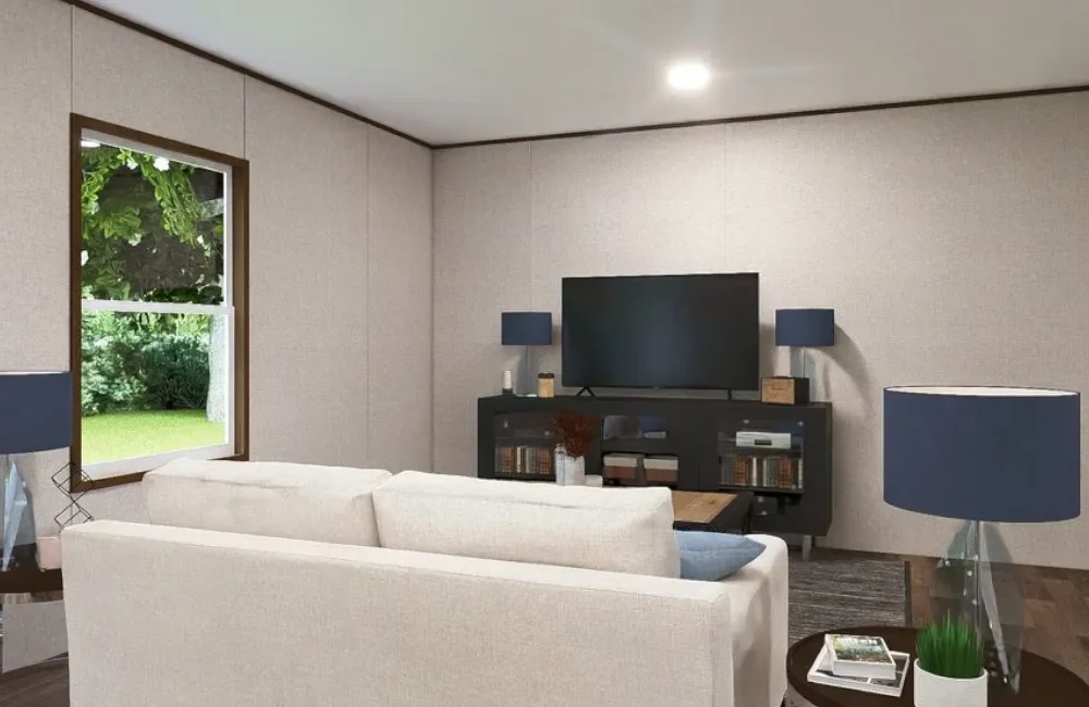 Living room with a cream sofa facing a media console, TV, and blue lamps, a window showing a green yard, and a side table with a lamp, books, and a potted plant.