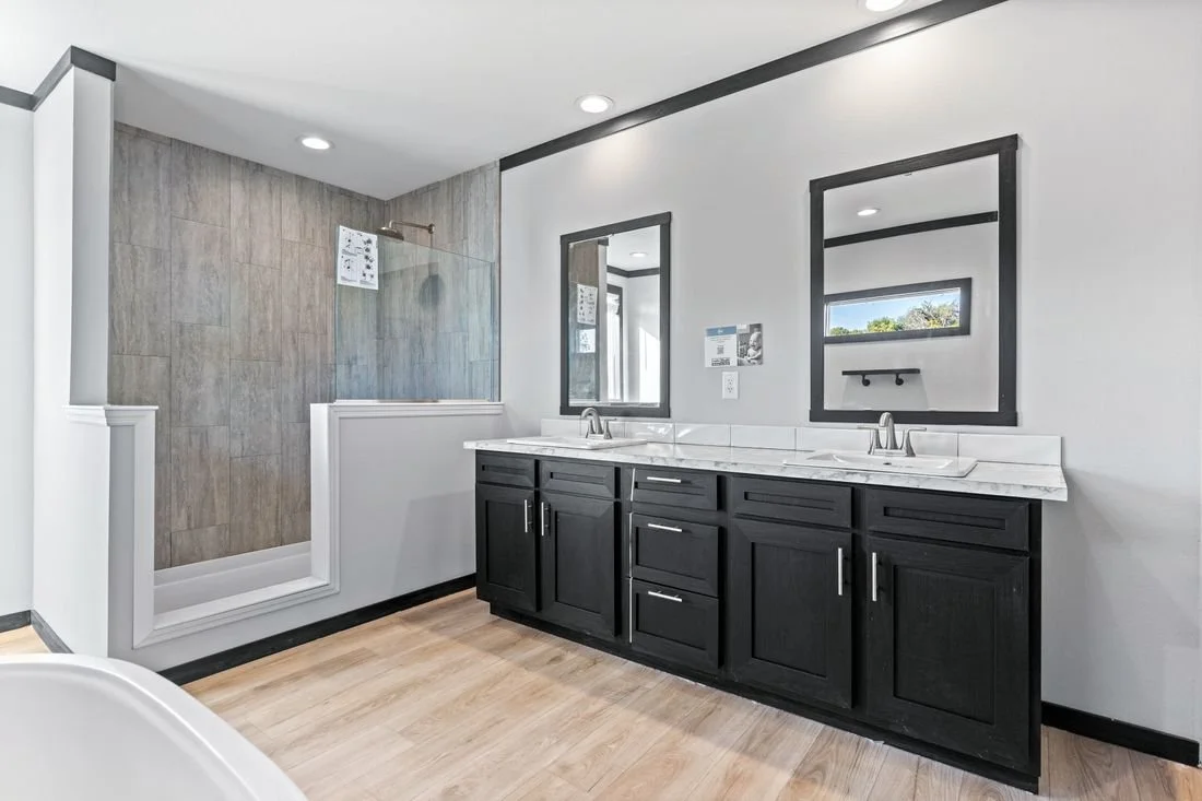 Modern bathroom with a double vanity, black cabinets, white countertops, two mirrors, and a walk-in shower with a glass partition.