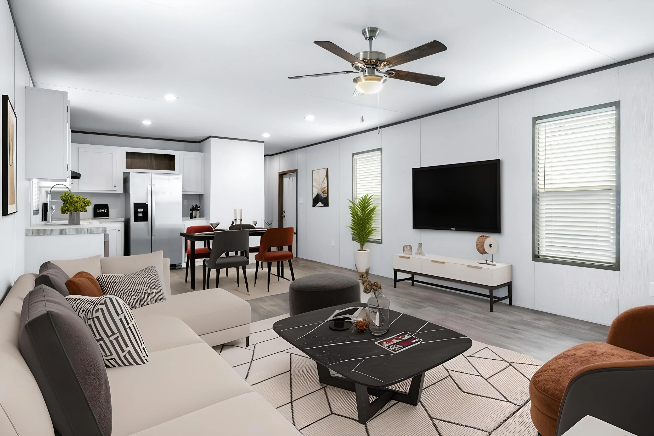 A modern living room with white walls, a beige sofa with patterned pillows, a black marble coffee table, and a brown armchair. There is a TV mounted on the wall, a white TV stand, and a potted plant. The space has windows with blinds and a ceiling fa
