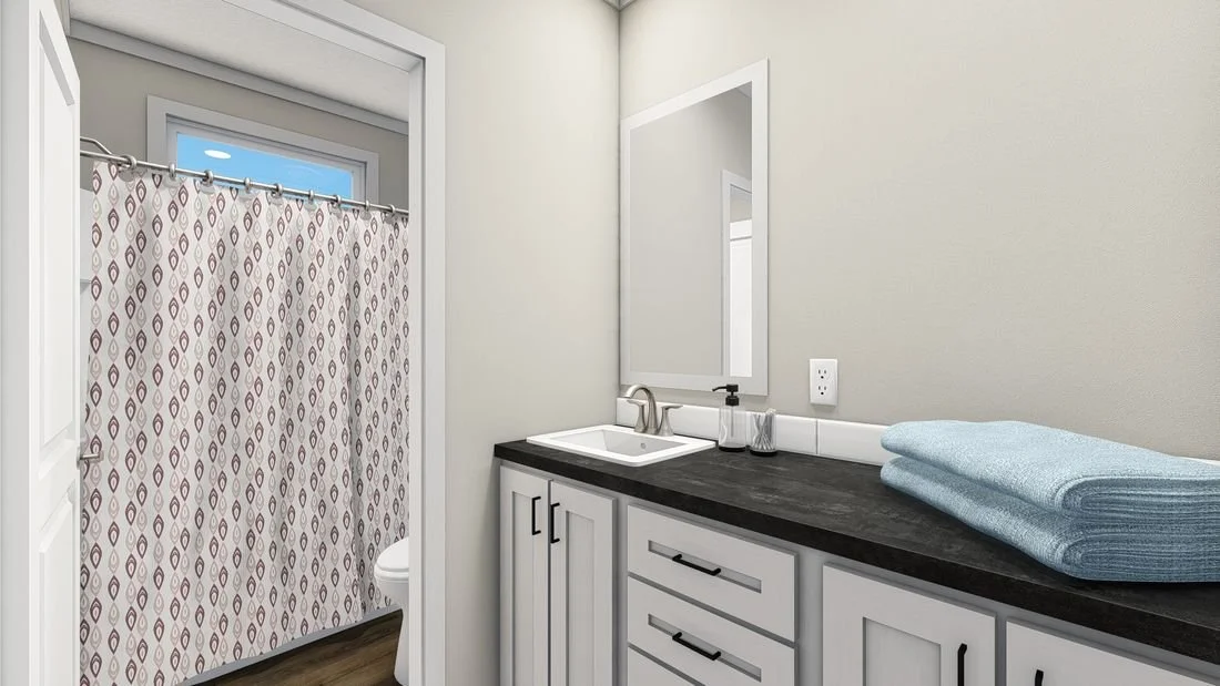 Bathroom with a white vanity, black countertop, mirror, and a shower with patterned curtain. Towels folded on the right side of the vanity.