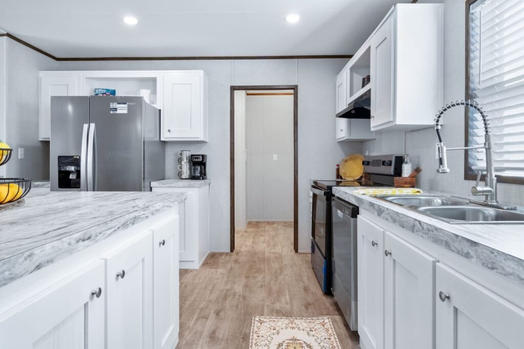 A modern kitchen with white cabinets, a marble countertop, stainless steel appliances, and a window with blinds.