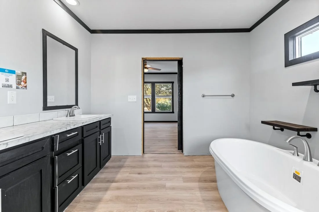 Empty bathroom with black cabinets, a white bathtub, and a window