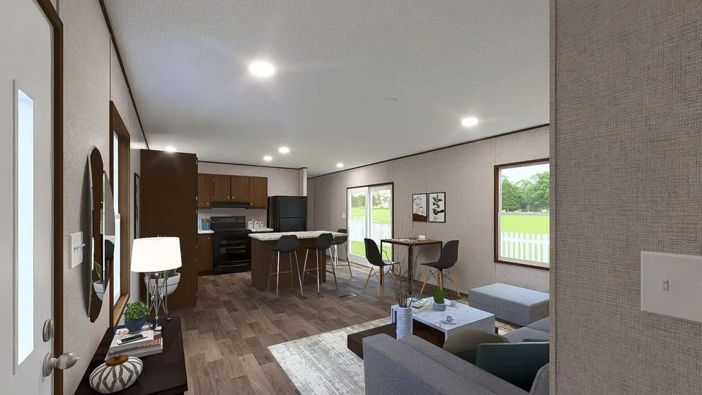 Open-concept living room and kitchen with hardwood floors, gray walls, a gray sofa, a coffee table, and a dining area with chairs. Large windows overlook a green yard.