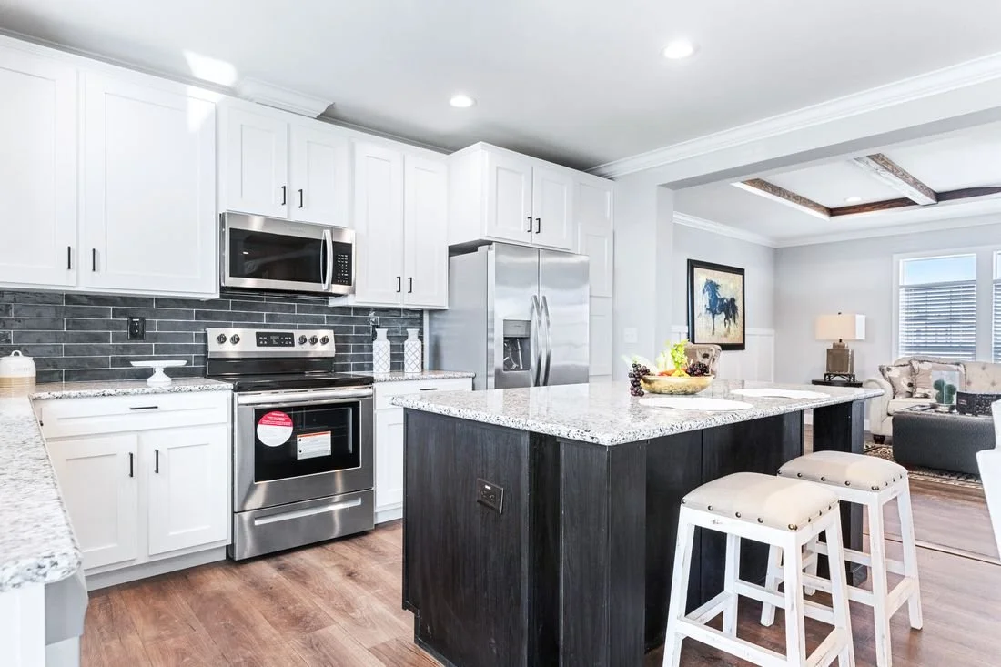 Modern kitchen with white cabinets, stainless steel appliances, a granite island, and a living area in the background.