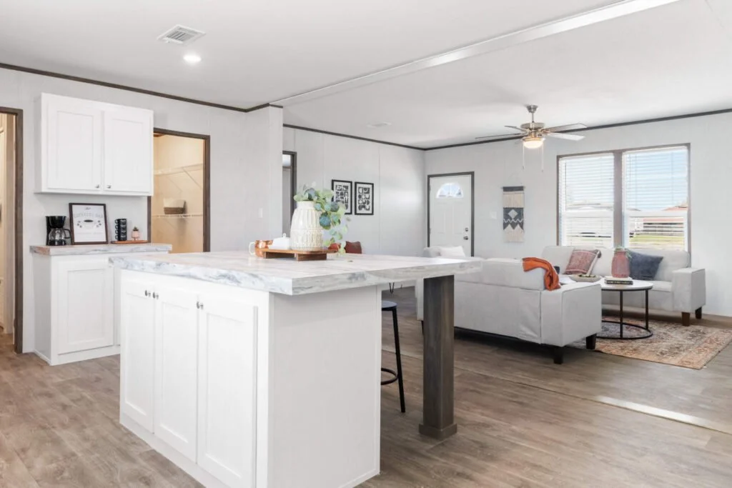 Open-concept living room and kitchen with white cabinetry, marble island, white sofa, and large windows in a modern home.