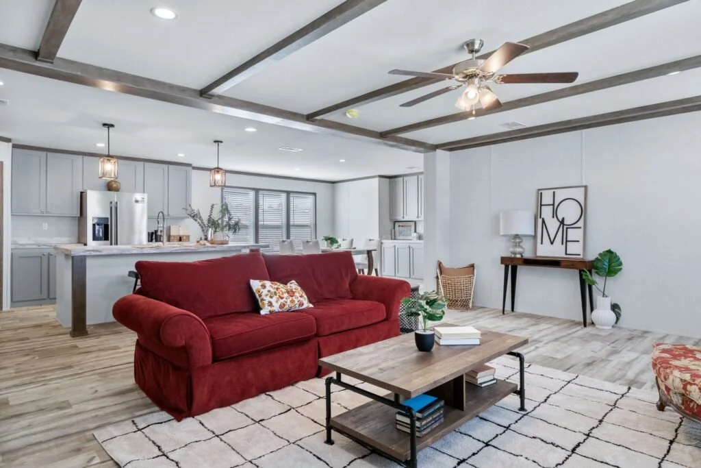 Open-concept living room and kitchen with a red sofa, wooden coffee table, and decor including a framed 'home' print, plants, and lights.