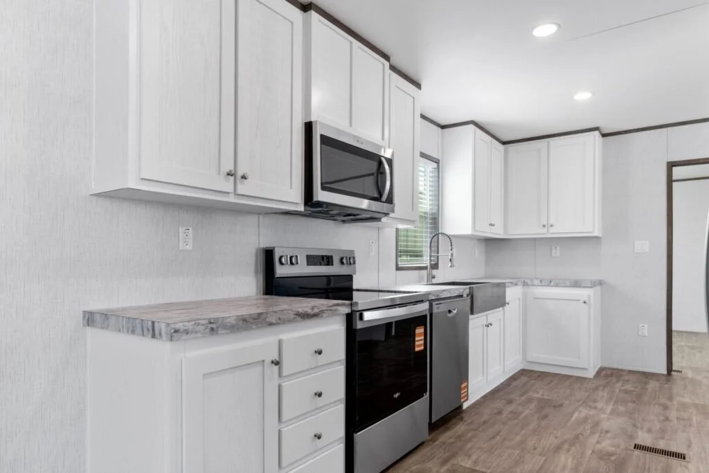 A modern kitchen with white cabinets, gray countertop, stainless steel appliances including a microwave, stove, and dishwasher, and a window above the sink.