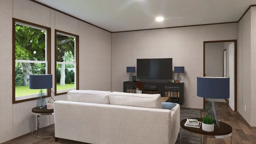 Living room with a cream sofa facing a black TV stand with a flat-screen TV, two blue lamps, and windows showing green trees outside.