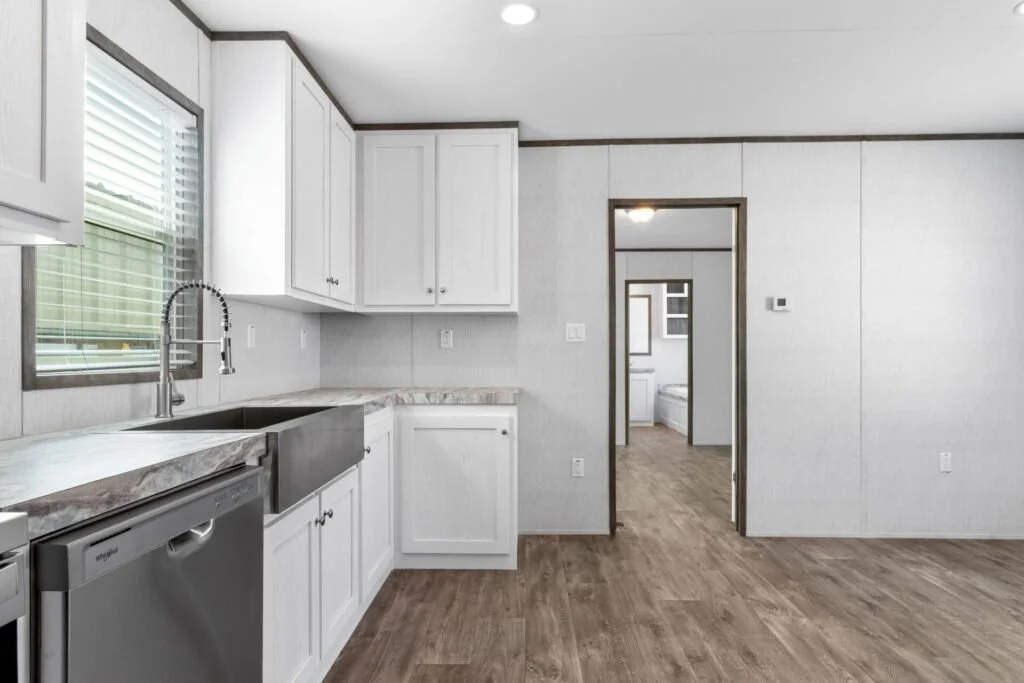 Kitchen with white cabinets, stainless steel sink, window with blinds, wood flooring, and an adjoining room with a washer and dryer.