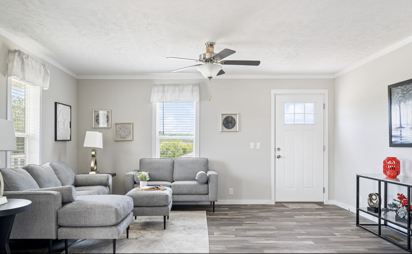 Bright living room with gray sofas, a black console table, and wall art, with white walls, wood-look flooring, and a ceiling fan.
