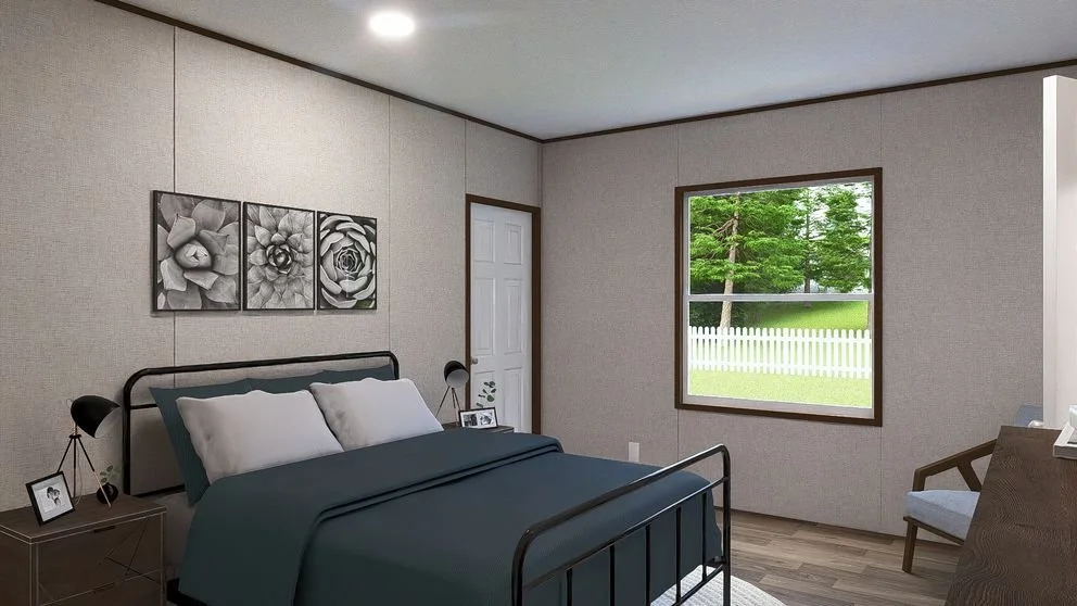 A minimalist bedroom with a black metal bed frame, dark teal bedding, and two white pillows. The wall above the bed has three black-and-white floral art prints. There is a side table with framed photos and a small lamp. A window looks out to a green 