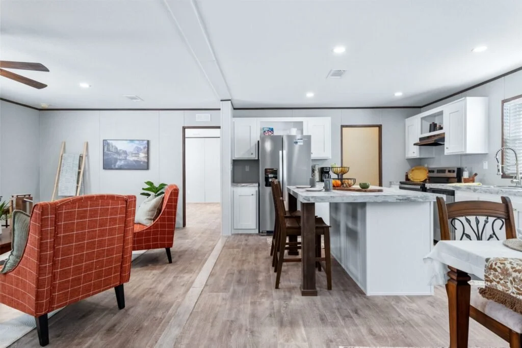 Open kitchen and living room with white cabinets, stainless steel fridge, island with bar stools, and orange upholstered armchairs.