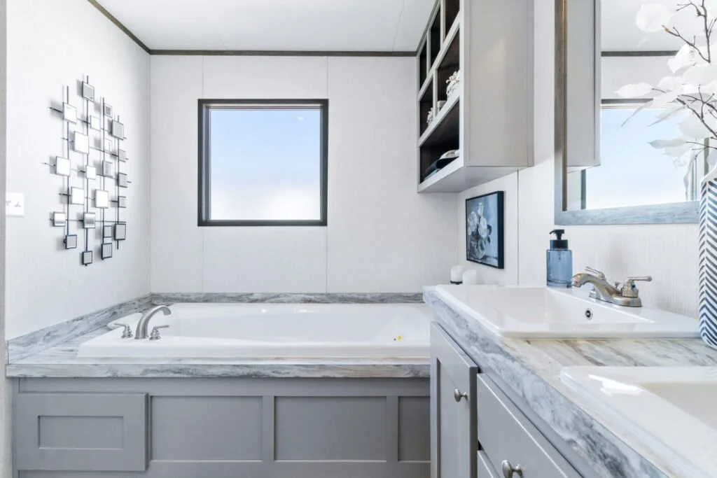 A modern bathroom with a bathtub, a window, a sink with marble countertop, and wall-mounted shelves with decorative items