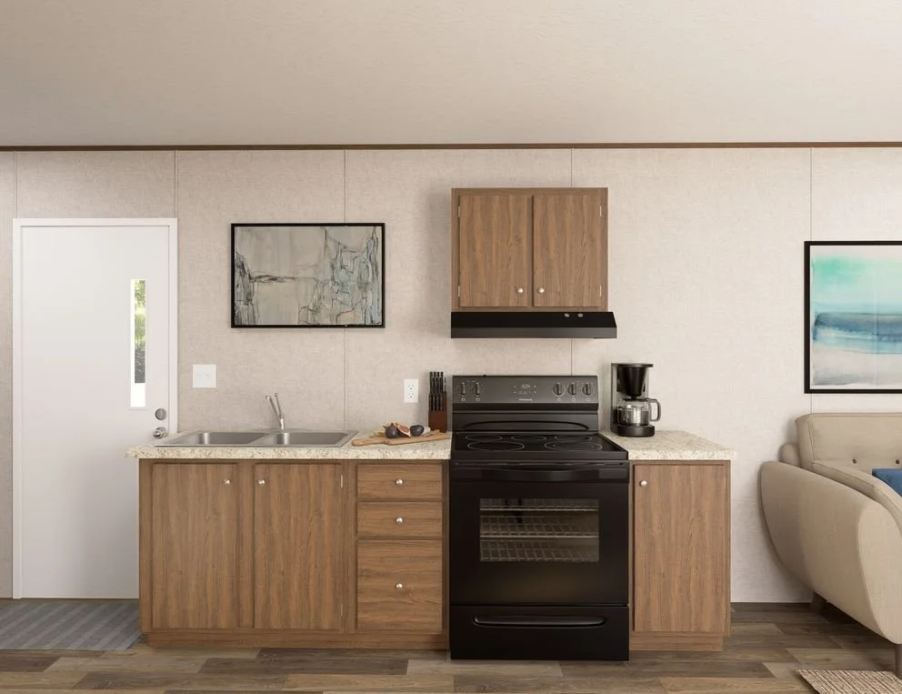 Kitchen with wooden cabinets, black stove, coffee maker, countertop, sink, framed artwork, gray wall, and part of a beige sofa visible on the right.