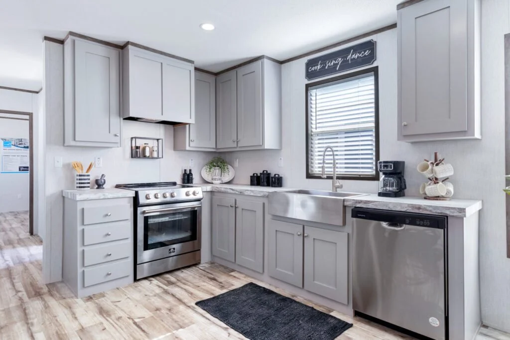 Modern kitchen with white cabinets, stainless steel stove and dishwasher, black countertop appliances, and a black window shade.