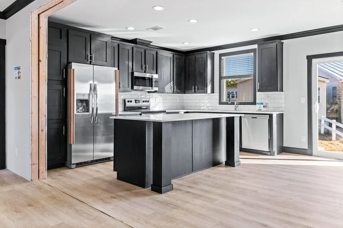 Modern kitchen with black cabinets, stainless steel refrigerator, microwave, and oven, white subway tile backsplash, island, window with blinds, and sliding glass door leading outside.