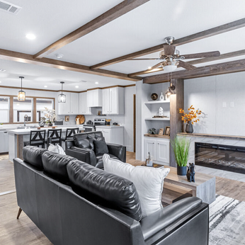Open-concept living room and kitchen with white cabinets, black furniture, and decorative plants.