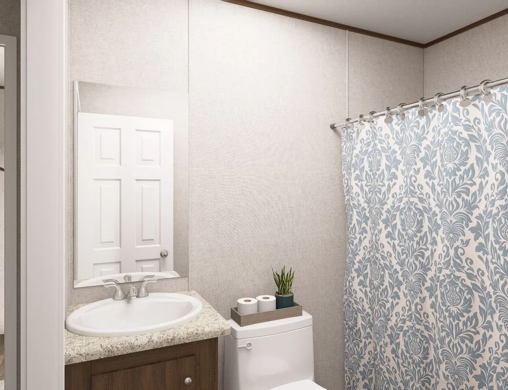 A small bathroom with a sink and mirror, toilet with a potted plant and toilet paper rolls on top, and a shower curtain with a blue and white floral pattern.