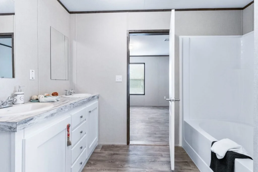 Bathroom with double sink vanity, marble countertop, towels, a bathtub with a towel, and a doorway leading to a room with a window.