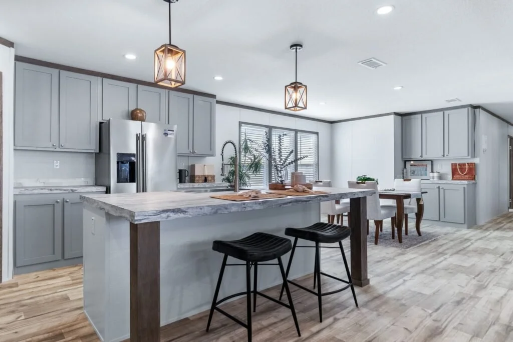 Modern kitchen with gray cabinets, marble countertop island, stainless steel refrigerator, and two hanging pendant lights.