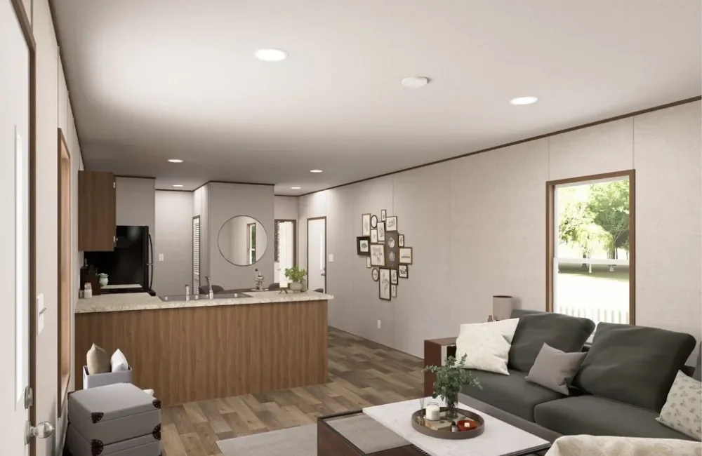 Living room with a gray sofa, pillows, a wooden side table, and a window with greenery outside. The room has wooden flooring and a gallery wall with picture frames.