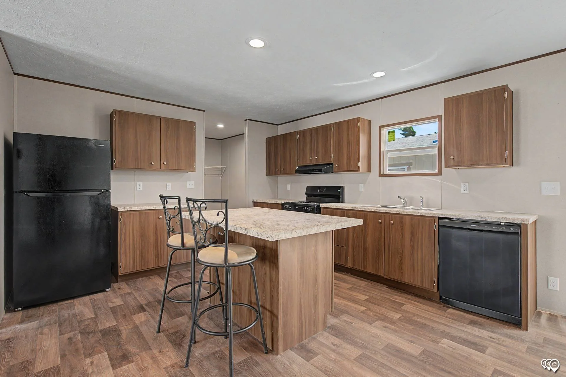 Kitchen with wooden cabinets, black refrigerator, black dishwasher, granite countertops, small window, and wooden barstools around an island.