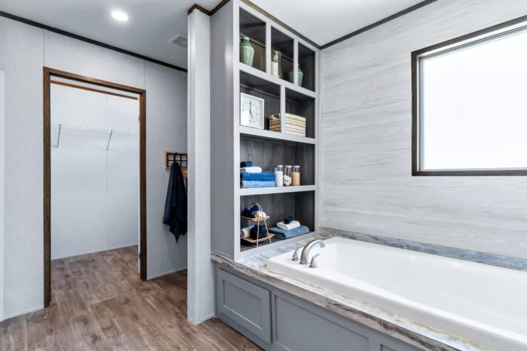 Bathroom with a bathtub next to a window and open shelving for towels and decor, with an adjacent walk-in closet.