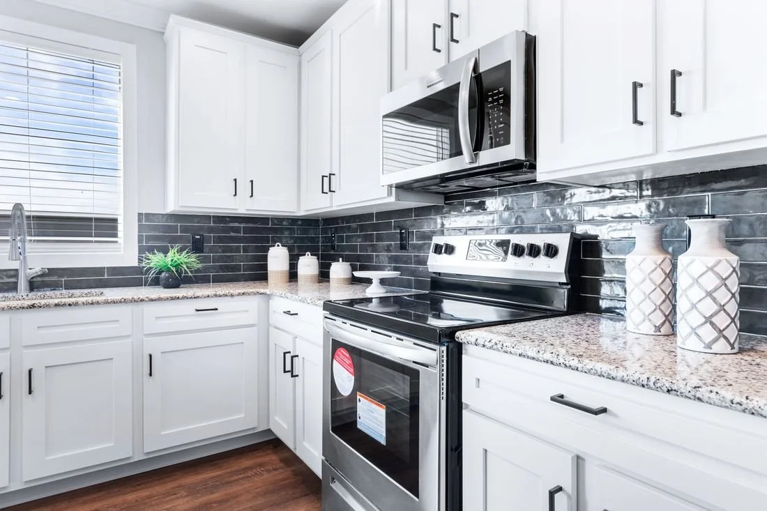 Modern kitchen with white cabinets, black backsplash, granite countertops, stainless steel microwave and stove, and decorative vases on the counter.