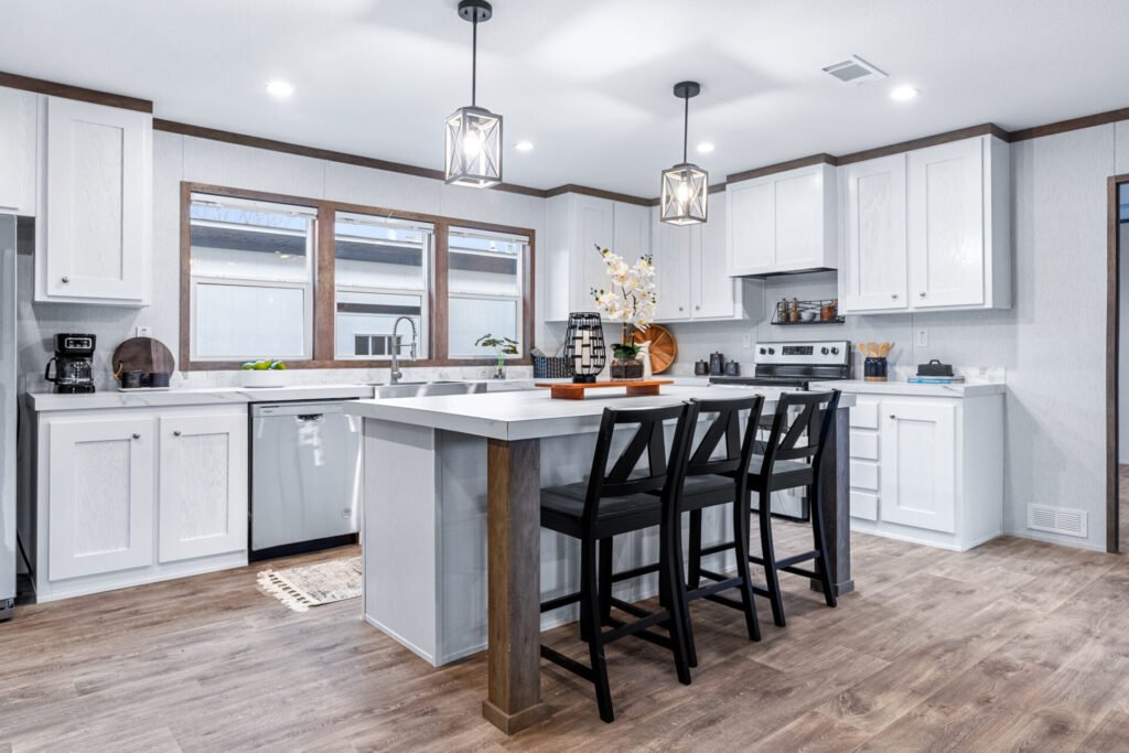 Modern kitchen with white cabinets, a white island with a gray base, black barstools, wood flooring, and natural light from large windows.