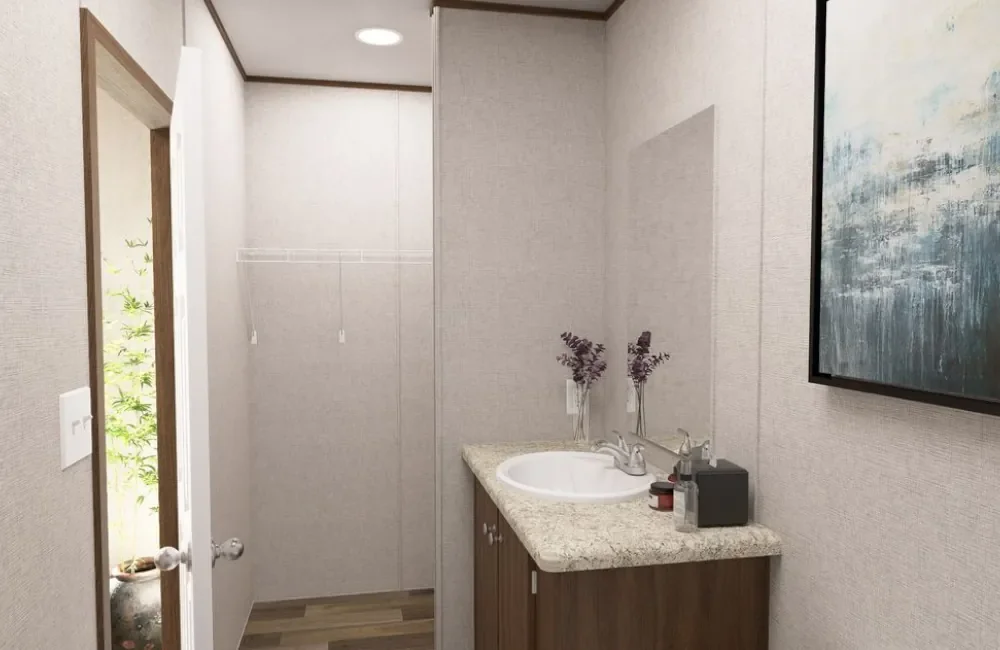Small bathroom with beige walls, granite countertop vanity with sink, a couple of vases with dried flowers, a painting on the wall, and an open door leading to a small outdoor area with greenery.