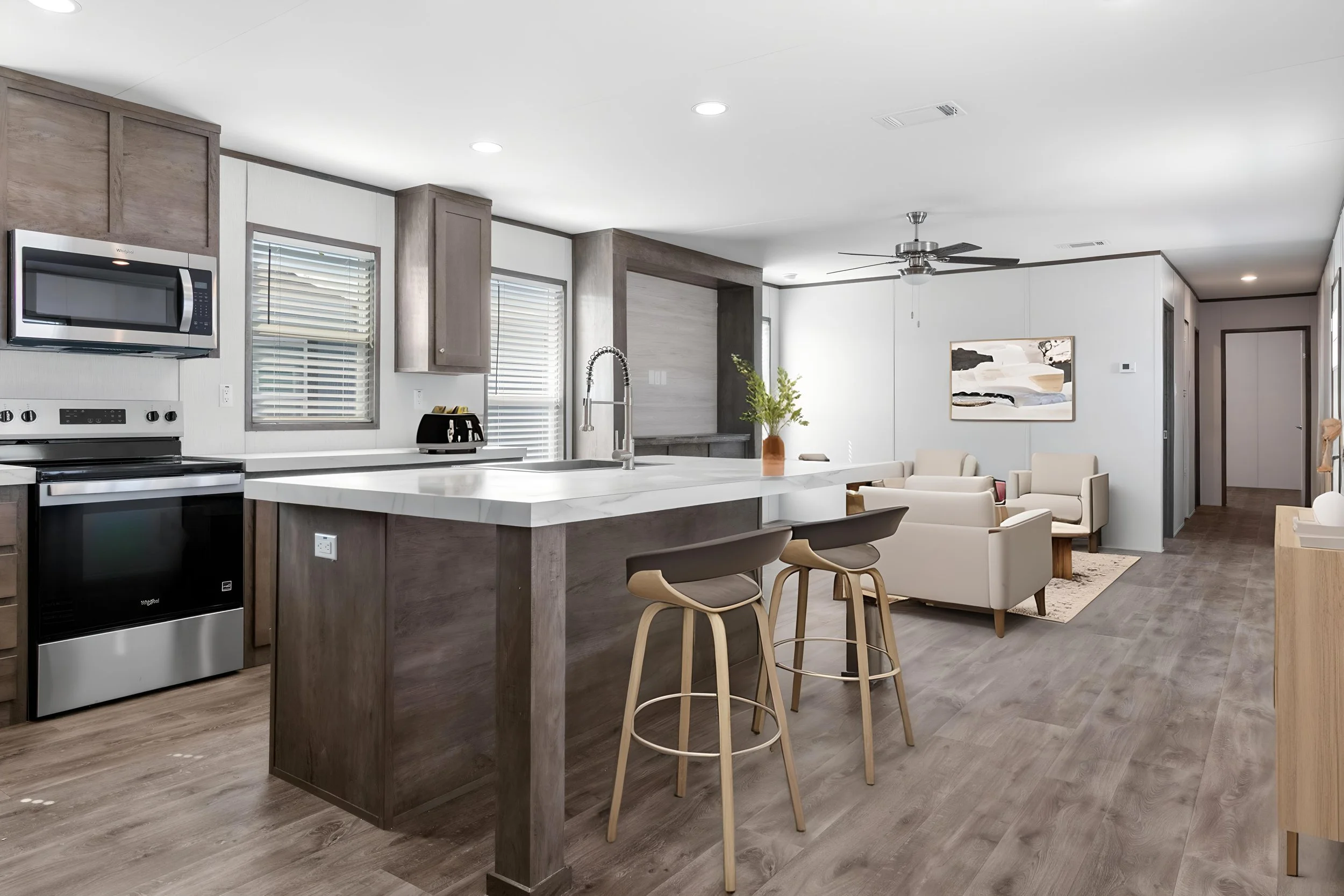 Modern open-concept kitchen and living room with gray and white color scheme, kitchen island with bar stools, stainless steel appliances, and seating area with armchairs and a wall art piece.