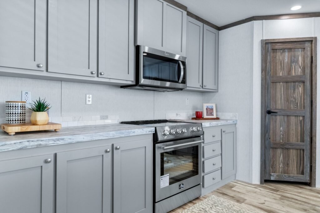 Modern kitchen with gray cabinets, a marble countertop, stainless steel microwave and oven, and a rustic wooden door.