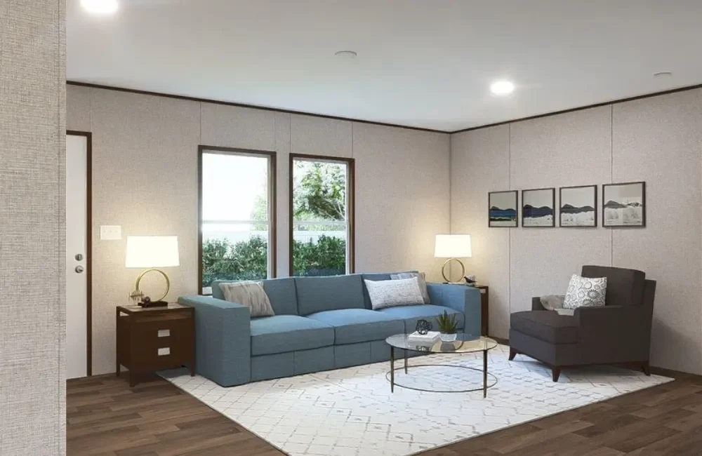 Living room with a blue sofa, gray armchair, glass coffee table, two side tables with lamps, framed artwork on beige wall, and a white rug on wood flooring.