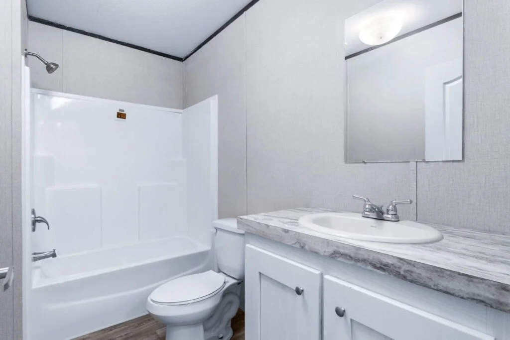Bathroom with a bathtub and shower, a toilet, and a sink with a marble countertop, a mirror, and light fixture above.