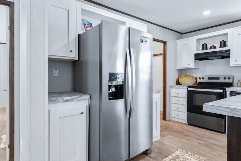 Kitchen with white cabinets and stainless steel refrigerator next to a marble countertop and a stove