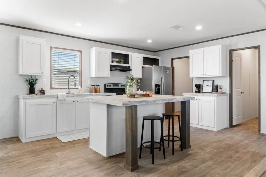 Modern kitchen with white cabinets, stainless steel appliances, a marble island, and wooden flooring.