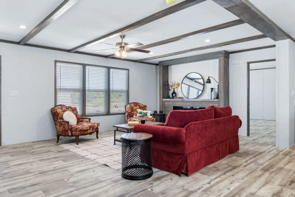 Living room with a red sofa, floral armchairs, wooden ceiling beams, and a large window with blinds.