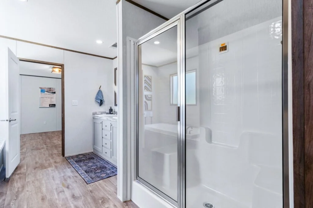View of a bathroom with a glass enclosed shower, white walls, wood flooring, and a white vanity with a mirror.