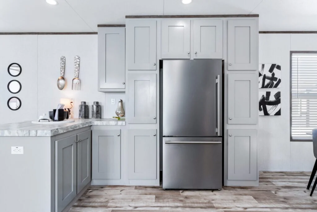 Modern kitchen with gray cabinets, stainless steel refrigerator, marble countertop, and wall decor including mounted spoons, forks, and circular art pieces.