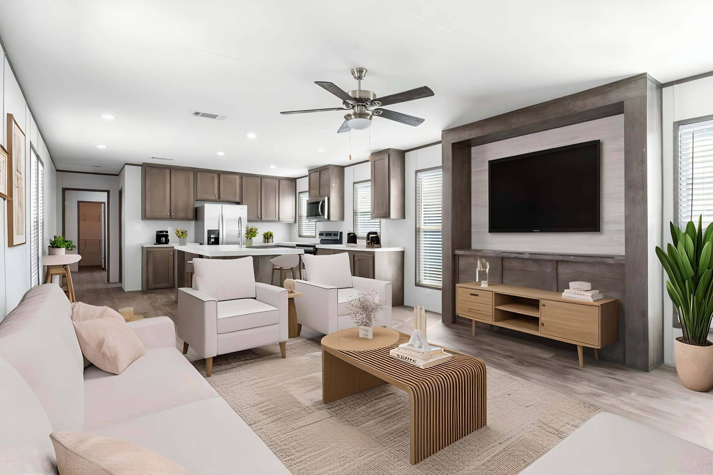Modern, open-concept living room and kitchen with neutral colors, white sofas, wooden furniture, a large flat-screen TV, and a ceiling fan.
