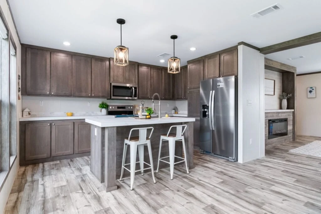 Modern kitchen with gray cabinetry, stainless steel appliances, a white island with bar stools, wood flooring, and pendant lighting.