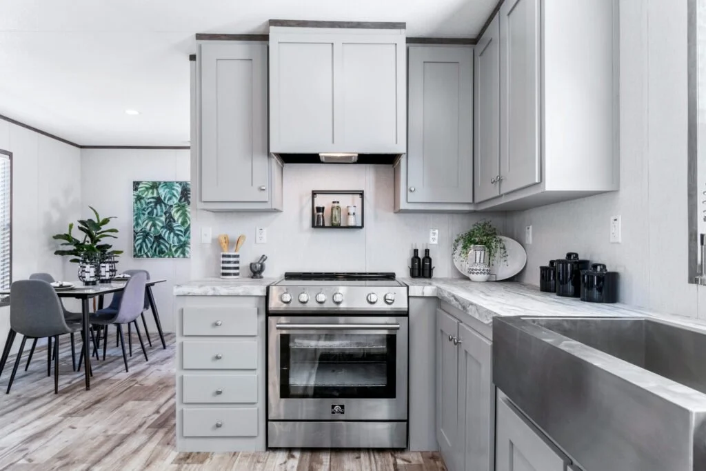 Modern kitchen with gray cabinets, stainless steel oven, marble countertops, black canisters, potted plant, and adjacent dining area with a round table and purple chairs