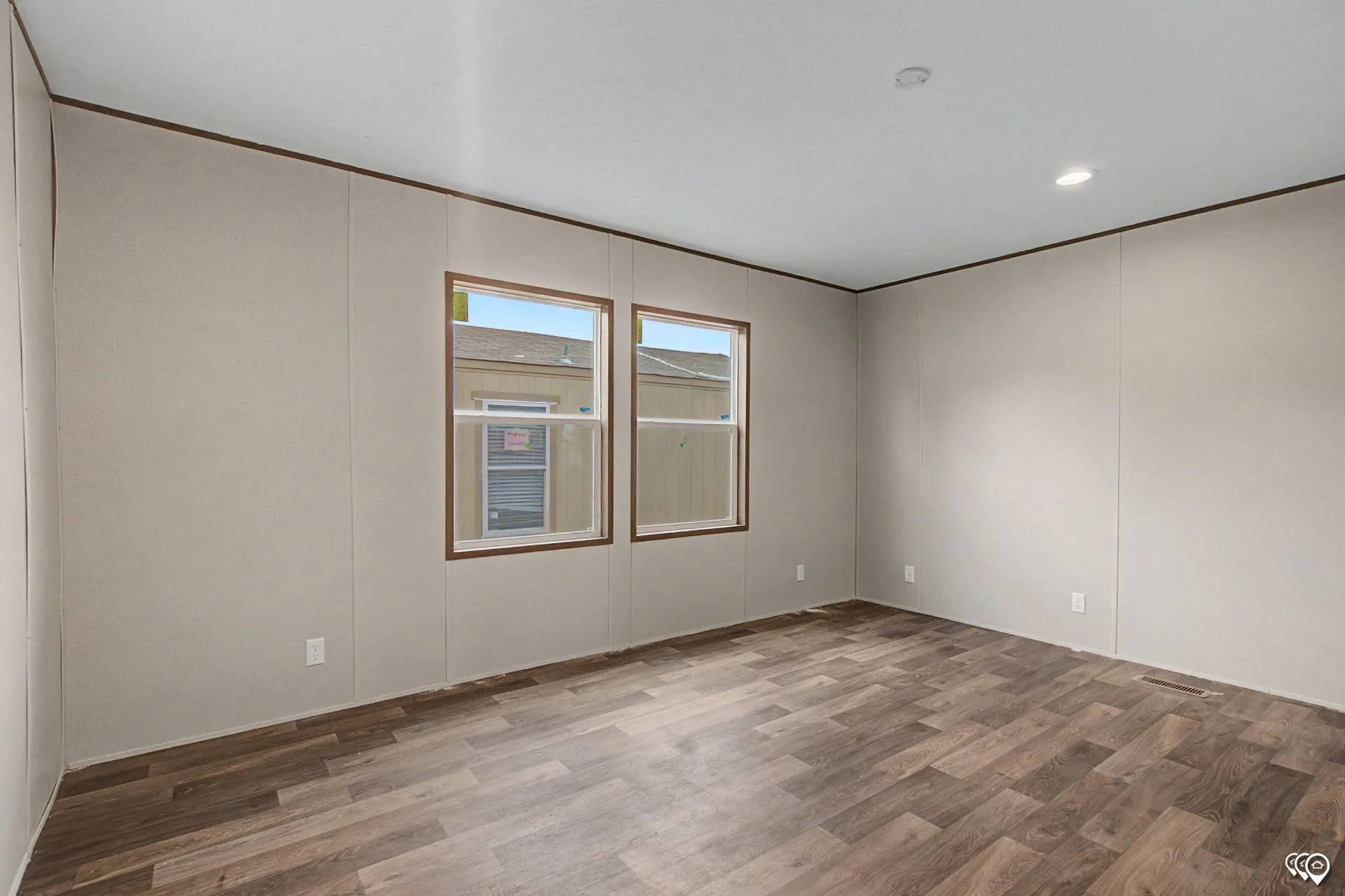 Empty room with beige walls, two windows, and wood-patterned flooring.