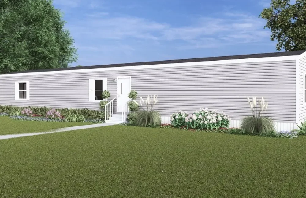 A white manufactured home with black roof, located in a yard with green lawn, pathway, and landscaped bushes and plants.